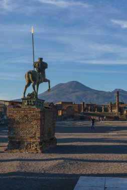 Günbatımında altın saat boyunca Forum 'un harabelerinde, arka planda Vesuvius Dağı, Pompeii, Campania, İtalya' da bronz bir heykel görülüyor.