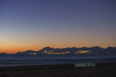Beyaz kayıklı kumsal ve alacakaranlıktan sonraki akşam karanlığında arka planda Amalfi Sahili 'ni aydınlatan Paestum, Campania, İtalya