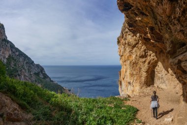 Akdeniz, San Vito Lo Capo, Sicilya, İtalya 'daki Monte Cofano Doğa Parkı' nın kayalık kıyı şeridinde mağarada duran yürüyüşçü.