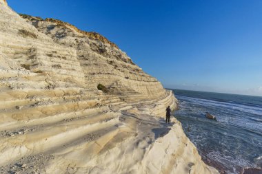 Günbatımının altın saatinde Akdeniz kıyısındaki kayalık uçurum merdivenlerinde yürüyen turistler, Realmonte, Sicilya, İtalya