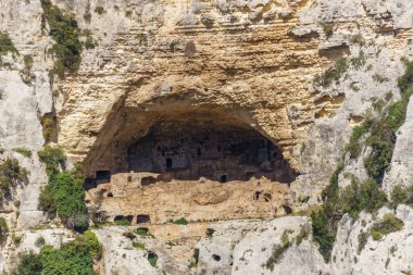 Prehistoric cave of necropolis carved in rock formation at canyon of Oriented Nature Reserve Cavagrande del Cassibile, Syracuse, Sicily, Italy clipart