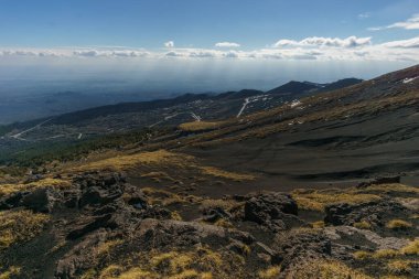 Volkanik Etna Dağı manzarası kara lav ve sarı çimlerle parçalı bulutlu bir kış günü, Catania, Sicilya, İtalya