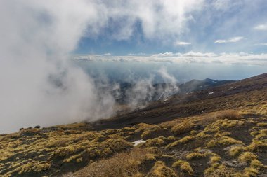 Volkanik Etna Dağı manzarası kara lav ve sarı çimlerle parçalı bulutlu bir kış günü, Catania, Sicilya, İtalya