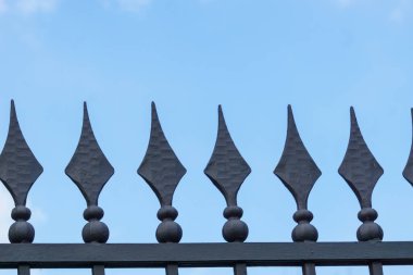 Mavi gökyüzüne karşı keskin elmas şekilli çivili metal çitler.