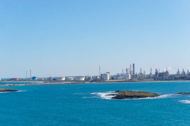 Güneşli bir günde, Brindisi, Puglia, İtalya 'nın Brindisi limanı yakınlarındaki sanayi bölgesi olan Pedagne' ye mavi deniz suyunun üzerinden bakın.