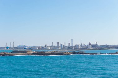 Güneşli bir günde, Brindisi, Puglia, İtalya 'nın Brindisi limanı yakınlarındaki sanayi bölgesi olan Pedagne' ye mavi deniz suyunun üzerinden bakın.