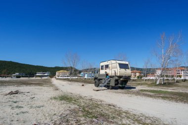 Motorhome on empty Ammoudia beach with village in background on a sunny spring day, Ammoudia, Epirus, Greece clipart