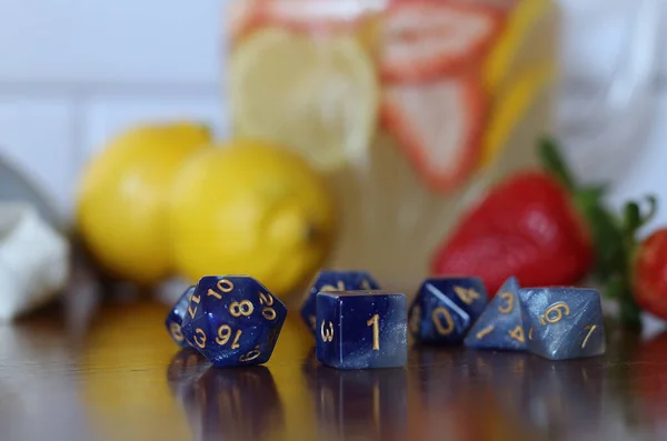 Close up of blue role playing dice with strawberry lemonade blurred in the background.