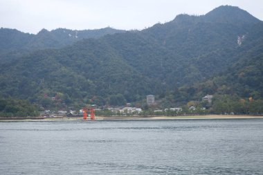 Looking at Miyajima island from the ferry. red giant Grand O-Torii gate stands beach on Winter, Hiroshima City, Hiroshima Prefecture, Japan