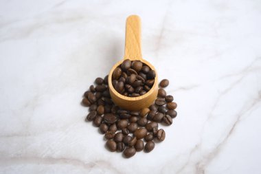 Kahve çekirdekleri tahta kaşıkta, kahve çekirdekleri beyaz zemine saçılmış.