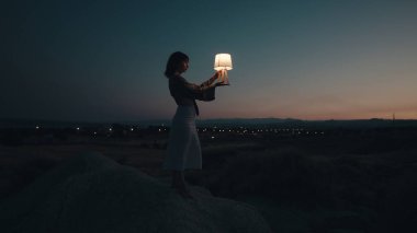 Genç bir kız güneş batarken batarken tepedeki kayalıklarda doğayla temas halinde.