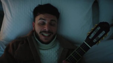 Man Playing a guitar in a bed 