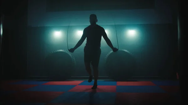 Fighter does some jump rope exercises in dark room under light.
