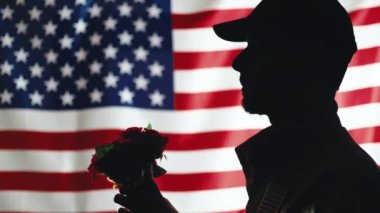 Usa askerinin silueti çiçekleri tutar.