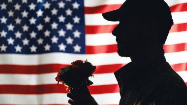 Usa askerinin silueti çiçekleri tutar.