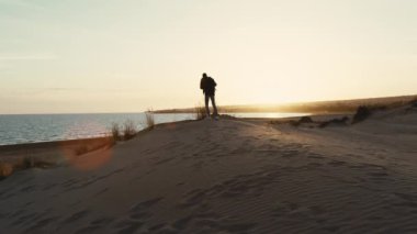 Gün batımında kum tepesindeki bir sırt çantalı adamın silueti