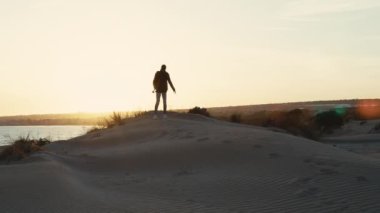 Gün batımında kum tepesindeki bir sırt çantalı adamın silueti
