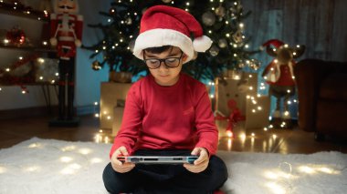 Noel ağacının altında video oyunları oynayan çocuk.