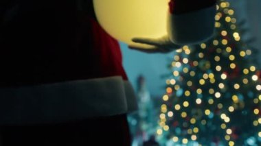 Noel Baba Noel ağacının altına ışık topu koyuyor. . 