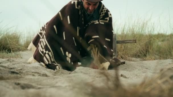 Man Met Poncho Graven Met Zijn Handen Het Zand — Stockvideo
