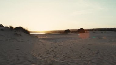 Gün batımında kum tepesindeki bir sırt çantalı adamın silueti