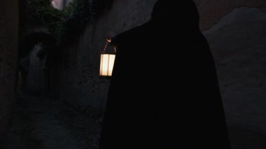 Koyu renk elbiseli bir adam ve yürüyen ve arayan bir fener. 