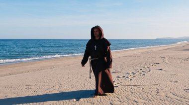 Kumlu sahilde çıplak ayakla yürüyen Hıristiyan bir rahip. . 