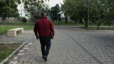 İşten sonra elinde bilgisayarla parkta yürüyen bir adam..