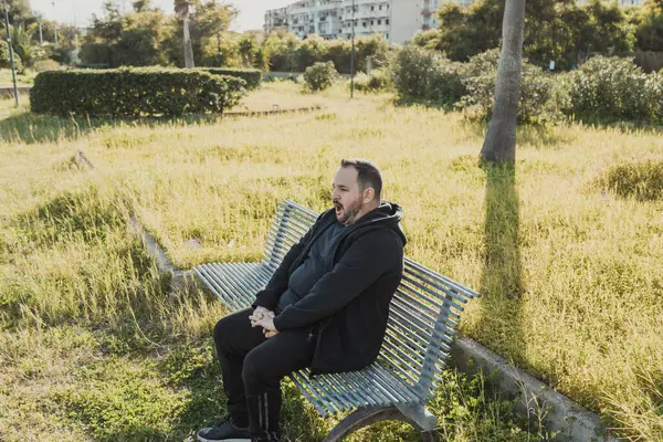 Sıkıcı adam bankta esniyor. . 