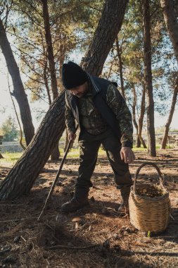 Kırsal doğada elinde sopa ve sepetle dolaşan bir adam. . 