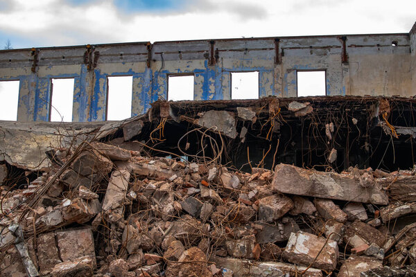 Demolition of an industrial building. In the foreground are the remains of broken reinforced concrete. In the background standing perimeter wall with windows.