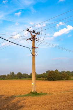 Mavi gökyüzü arkaplanlı bir alanda yüksek voltajlı elektrik hatları.