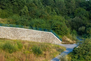 A masonry retaining wall made of stone that prevents landslides onto the asphalt road. clipart