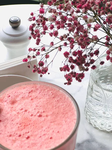 Smoothie bardağının ve açık bir kafedeki masada duran küçük pembe çiçeklerin yakın çekimi..