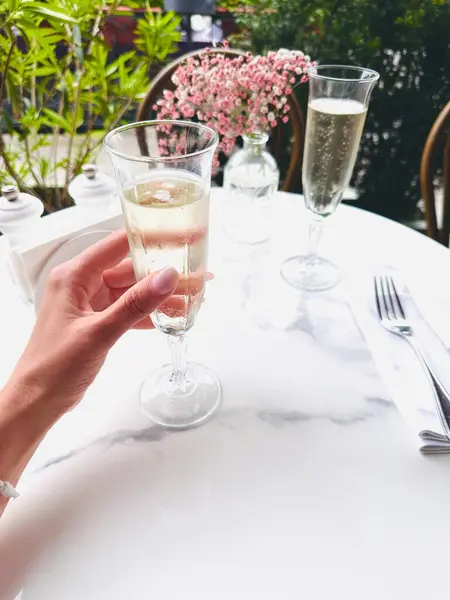 Kafkasyalı bir kızın elinde bir bardak şampanya, dışarıdaki kafede bir masada.. 