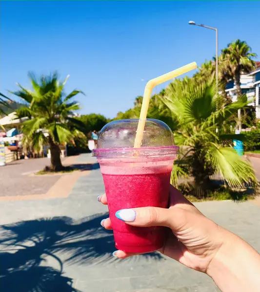 Genç bir kızın elinde, palmiye ağaçlarının arka planında meyve püresi.. 