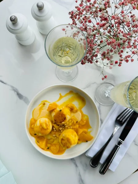 Mango gözlemeleri, yanında dilimlenmiş mango, açık kafedeki masada iki kadeh şampanya..