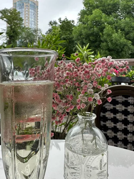 Caddedeki bir kafede masanın üstüne iki bardak şampanya ve pembe çiçek koy. . 