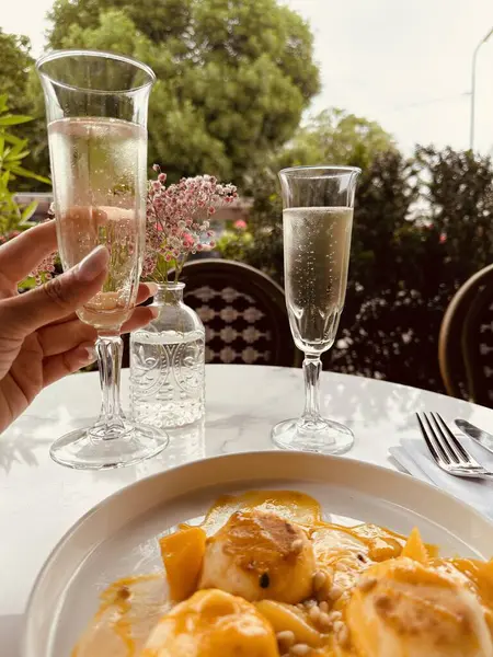 Yanında dilimlenmiş olgun mangolu mango, açık kafedeki masada iki bardak köpüklü şarap.. 