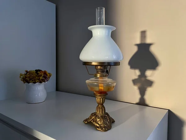 Beautiful vintage oil lamp with lamp shade made of white glass on a white cabinet. Shadow of the lamp on the wall. Modern interior design using an antique element. High quality photo