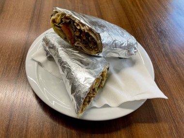 Tahta bir masaya folyoya sarılı nefis bir shawarma ile beyaz tabak. Lezzetli Orta Doğu yemekleri. Otantik sokak yemekleri. Yüksek kalite fotoğraf