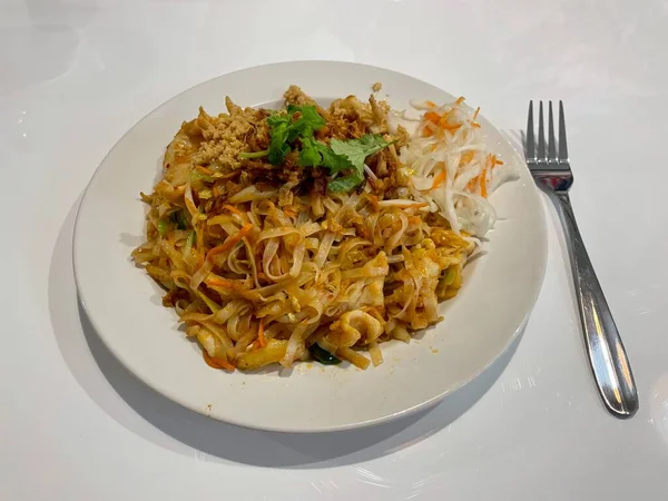 Freshly prepared Thai fried noodles with chicken and vegetables garnished with coriander and peanuts on a white plate. High quality photo