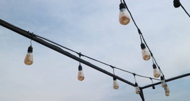 Telli ampuller açık gökyüzünün altında asılı.