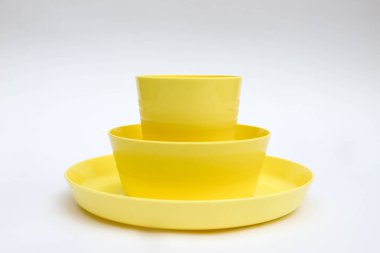 Sarı plastik yemek takımı, kase, tabak ve bardak beyaz arka planda izole edilmiş.