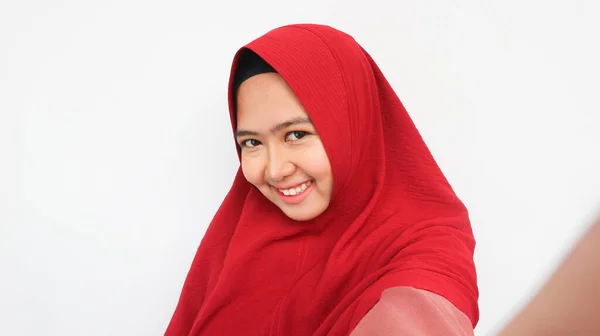 笑顔若いですアジアのイスラム教徒女性で赤いヒジャーブあります自画撮り携帯電話絶縁上の白い背景 — ストック写真
