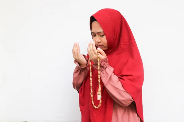 Asian Muslim woman in headscarf and hijab prays with her hands up in air with holding pray beads. Indonesian woman. Religion praying concept isolated on white background.