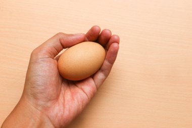 Elle tutulan tavuk yumurtası kahverengi ahşap arka planda izole edilmiş.