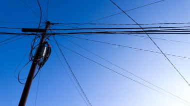 Genişletilmiş ve düzensiz kablolu uzun elektrik direkleriyle açık mavi gökyüzü manzaralı.