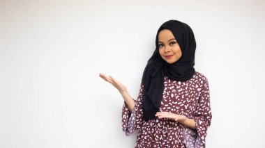 Asyalı tesettürlü genç bir kadın izole edilmiş beyaz arka plan üzerine davet edilmek için ellerini yana uzatıyor.