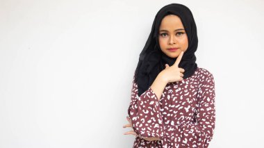 Asyalı tesettürlü genç bir kadın, izole edilmiş beyaz bir arkaplanda rahatsız görünürken bir fikir düşünüyor.